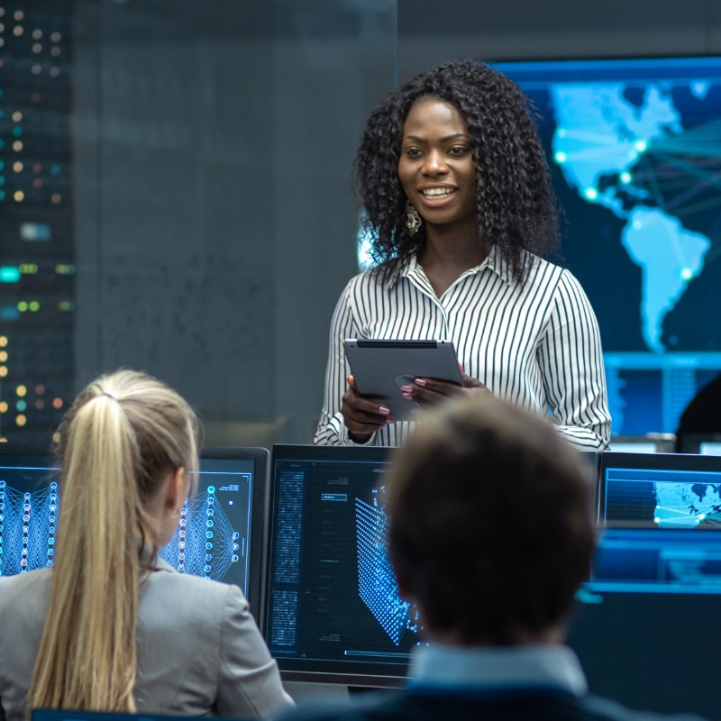 A woman speaking to a group of collegues in a command center