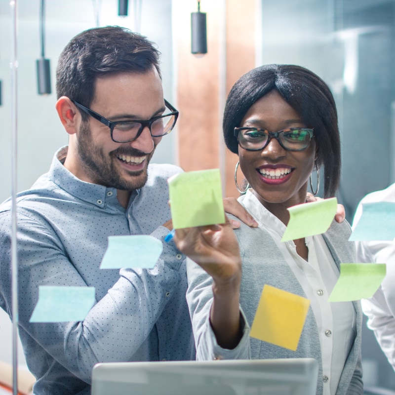 Two workers looking at sticky notes on a window
